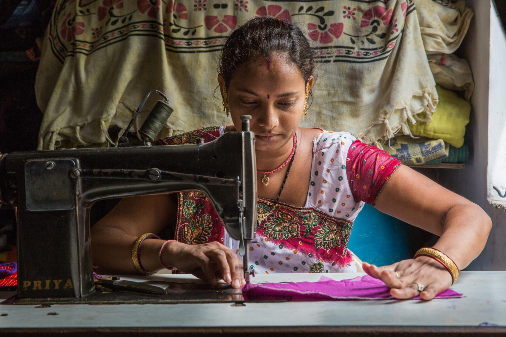 An Indian woman sits at a sewing machine, stitching a purse