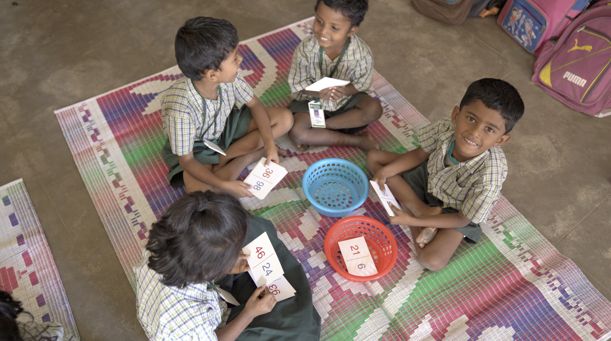 Children in an India classroom sit in a circle on the floor and play a math learning game.