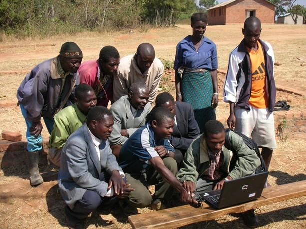 Farmers in Malawi gather around a laptop to learn about fingerprinting technology.