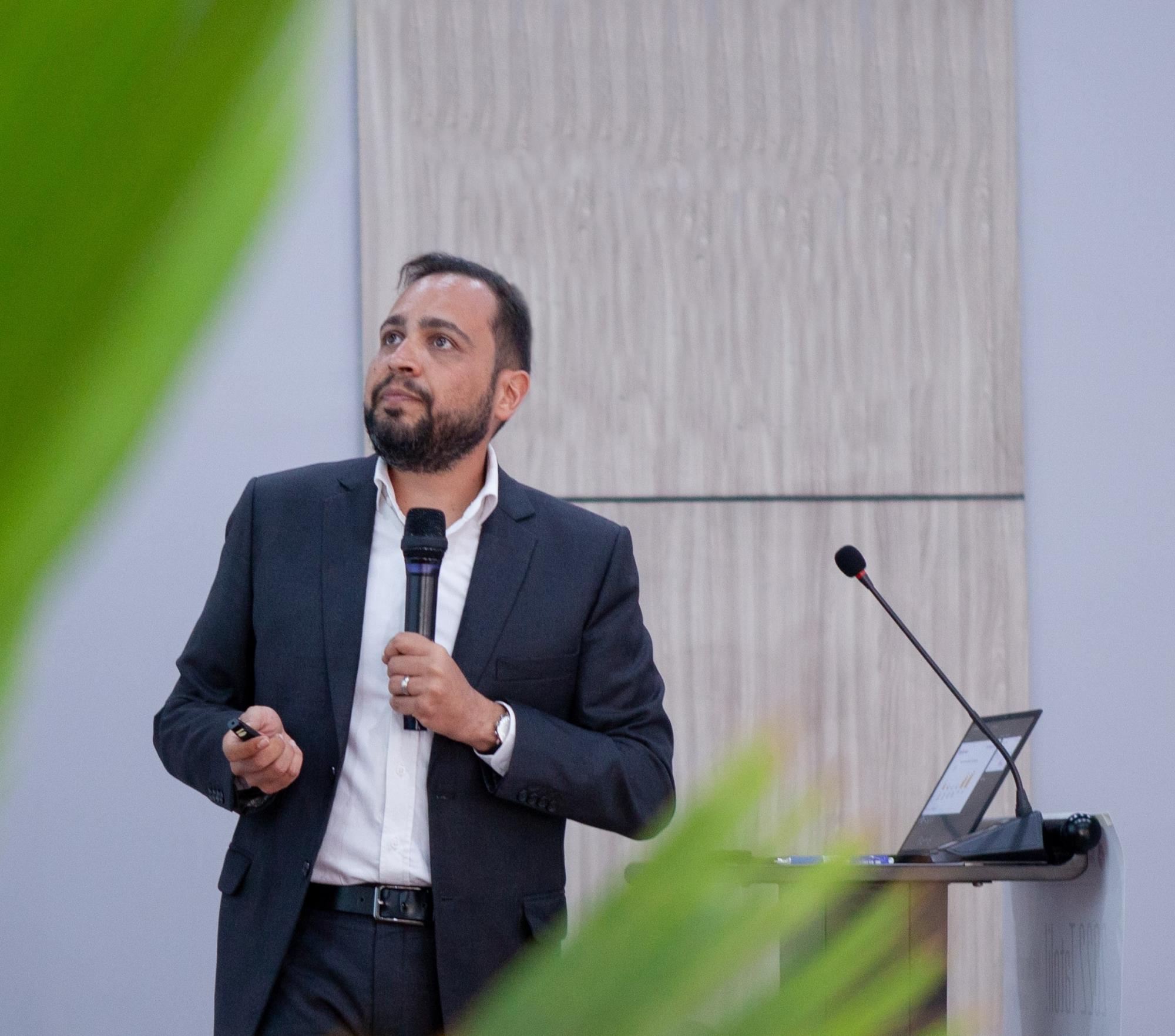 A man in a suit stands at a podium holding a microphone.
