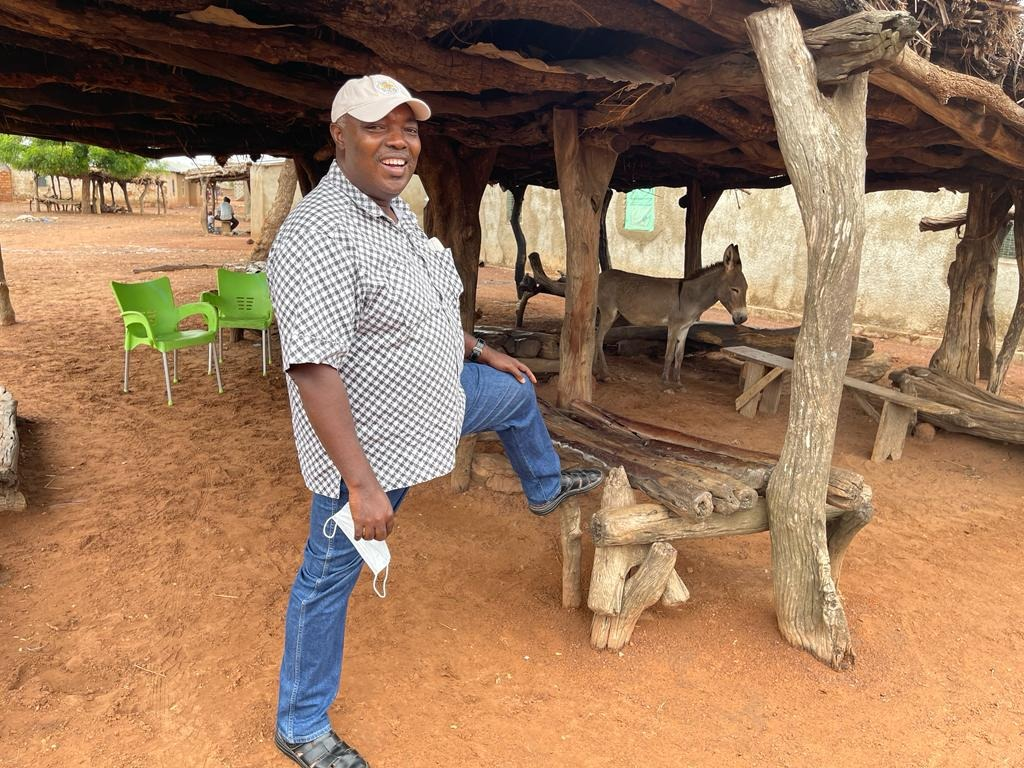 Robert Darko Osei stands under a wood structure with a mule in the background.