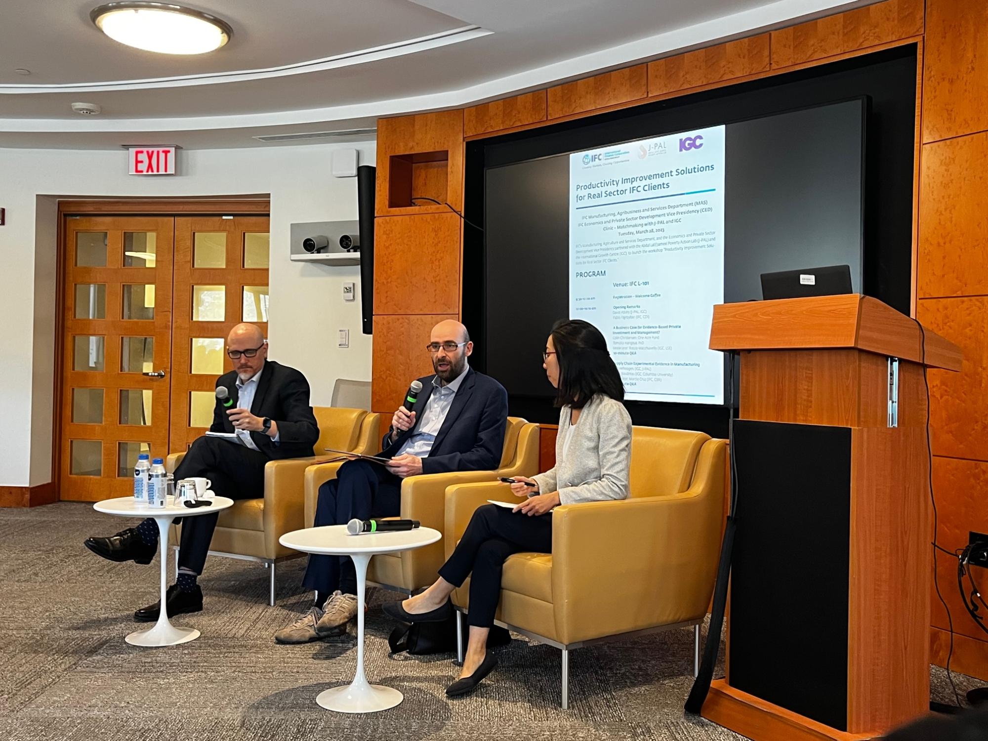 Two men and one woman sit in chairs on a panel.
