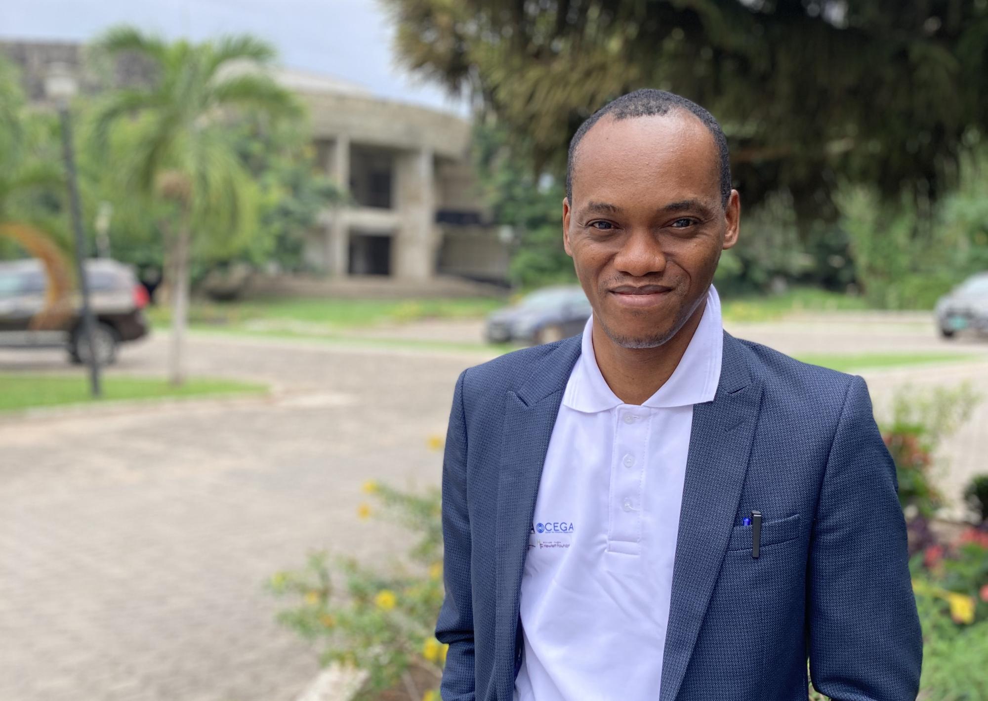 A headshot of a man in a suit jacket with trees in the background.