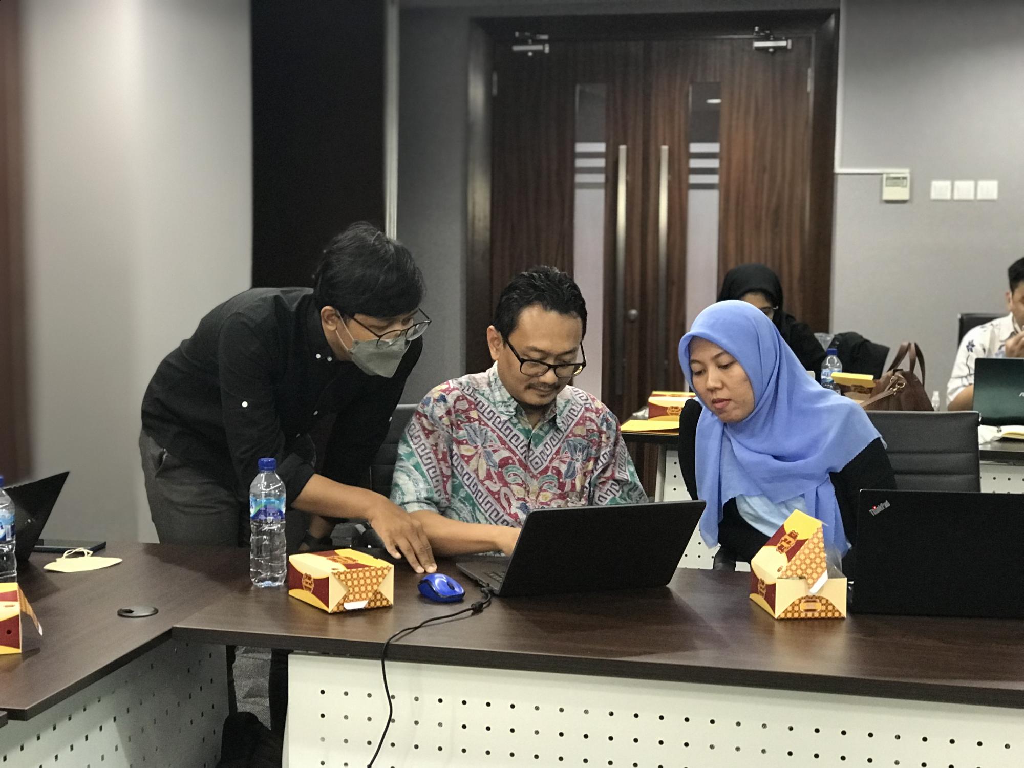 Two men and one women sit and look at a computer.