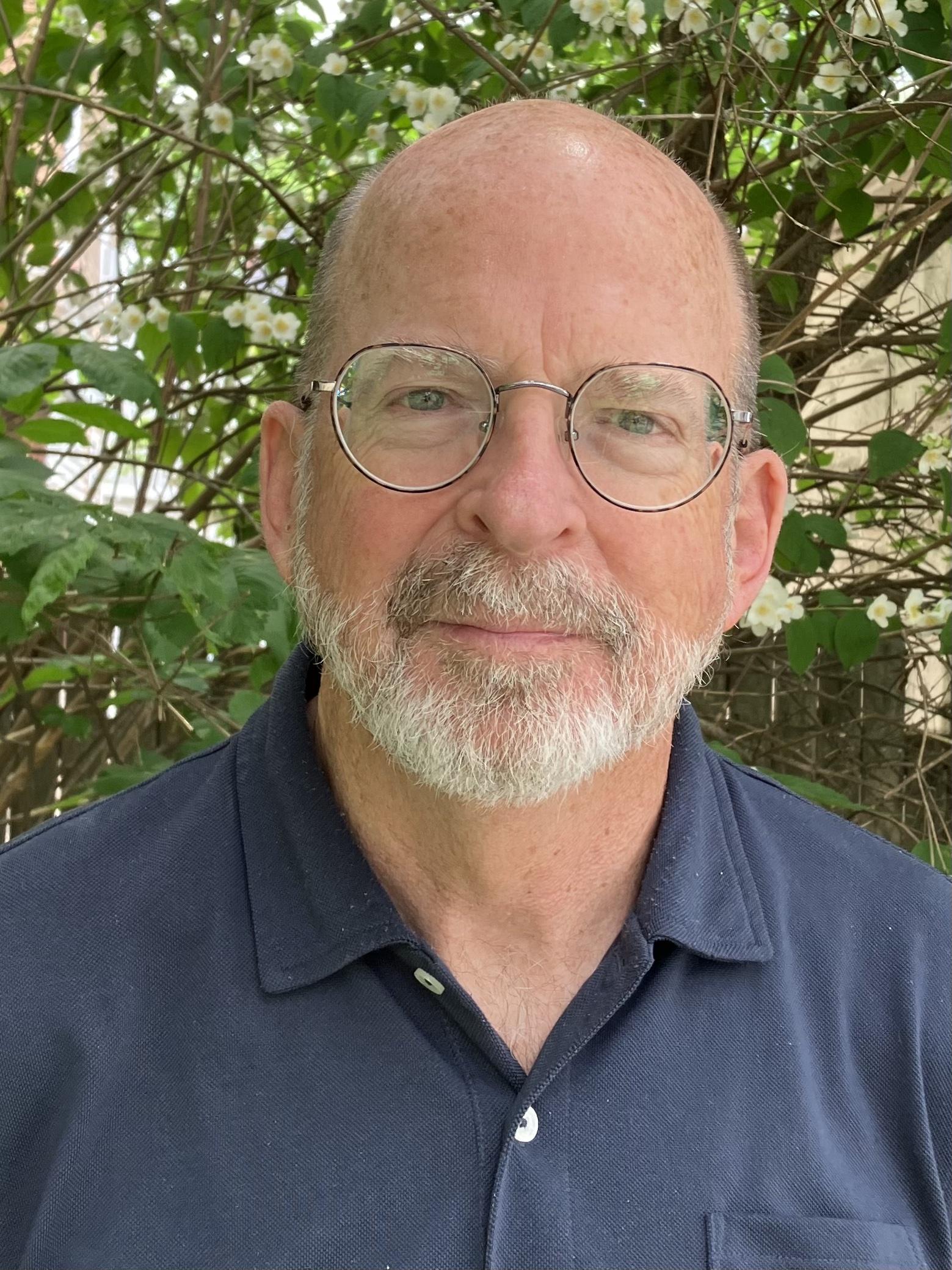 Head shot of a man with a blue shirt and glasses.