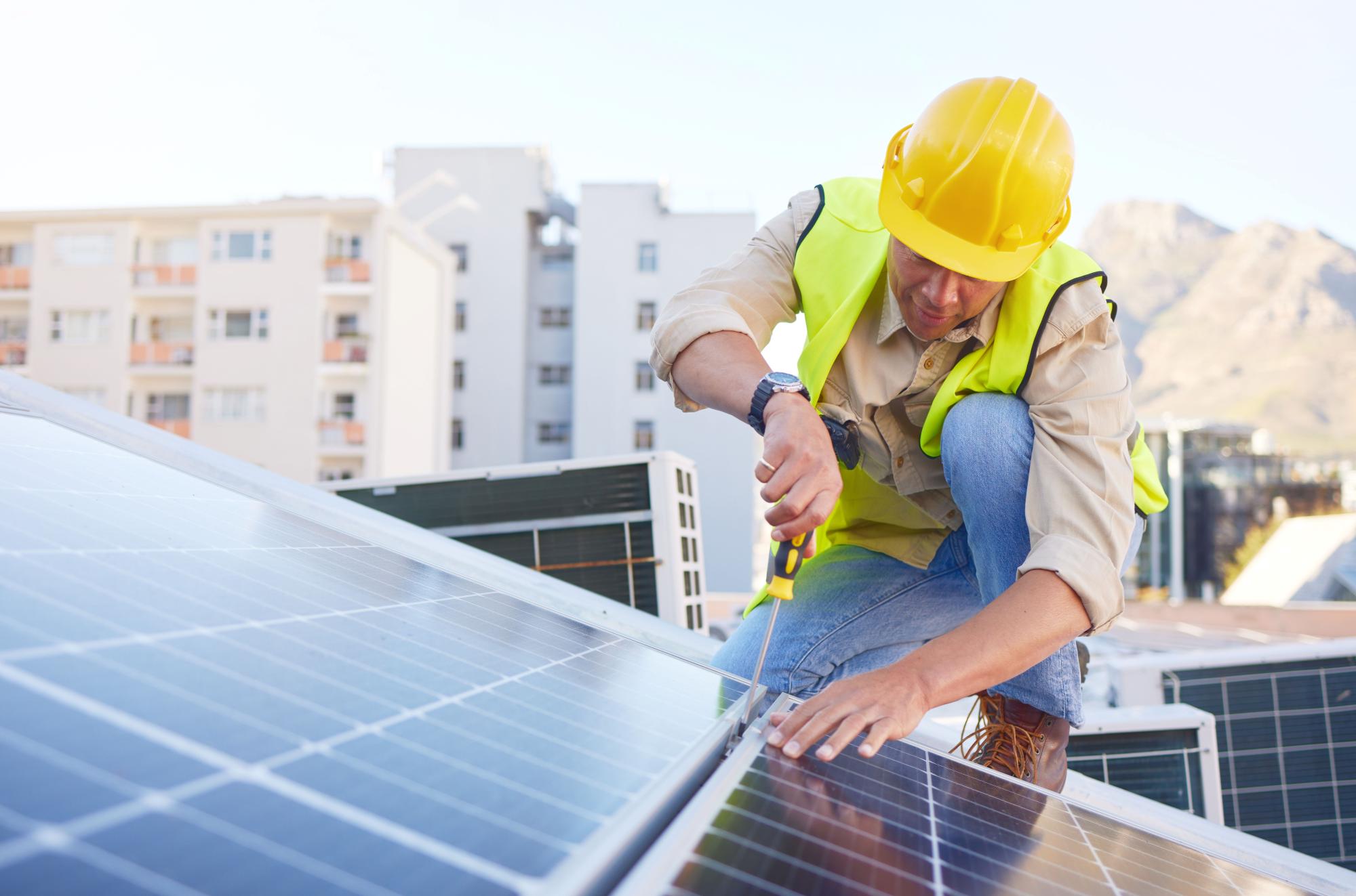 A man installs a solar panel on a rooftop on a sunny day.