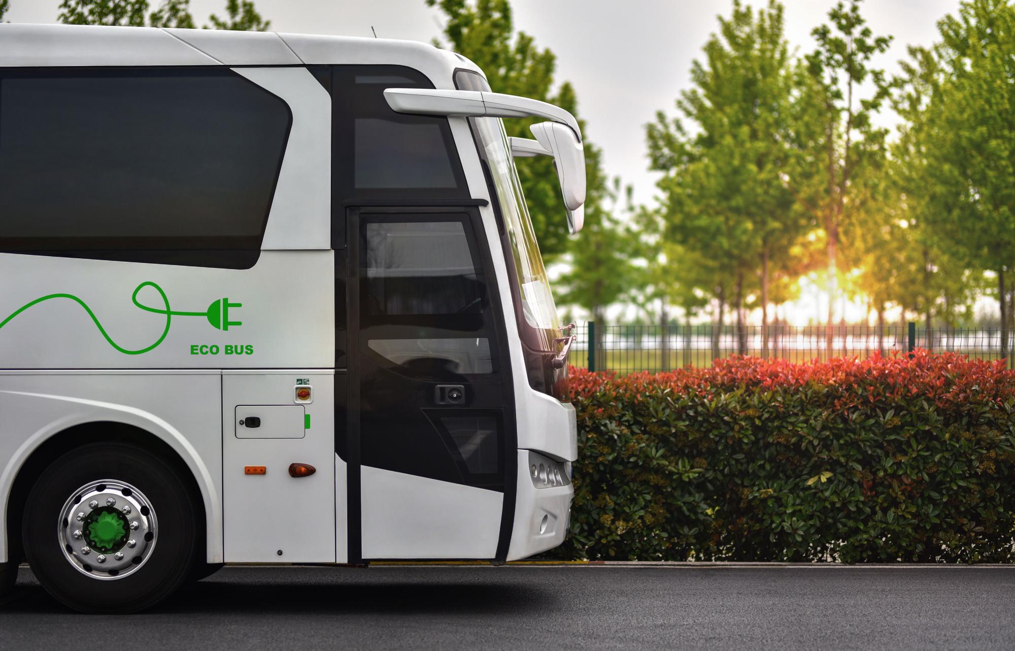 White electric shuttle bus drives down a tree-lined street at sunset