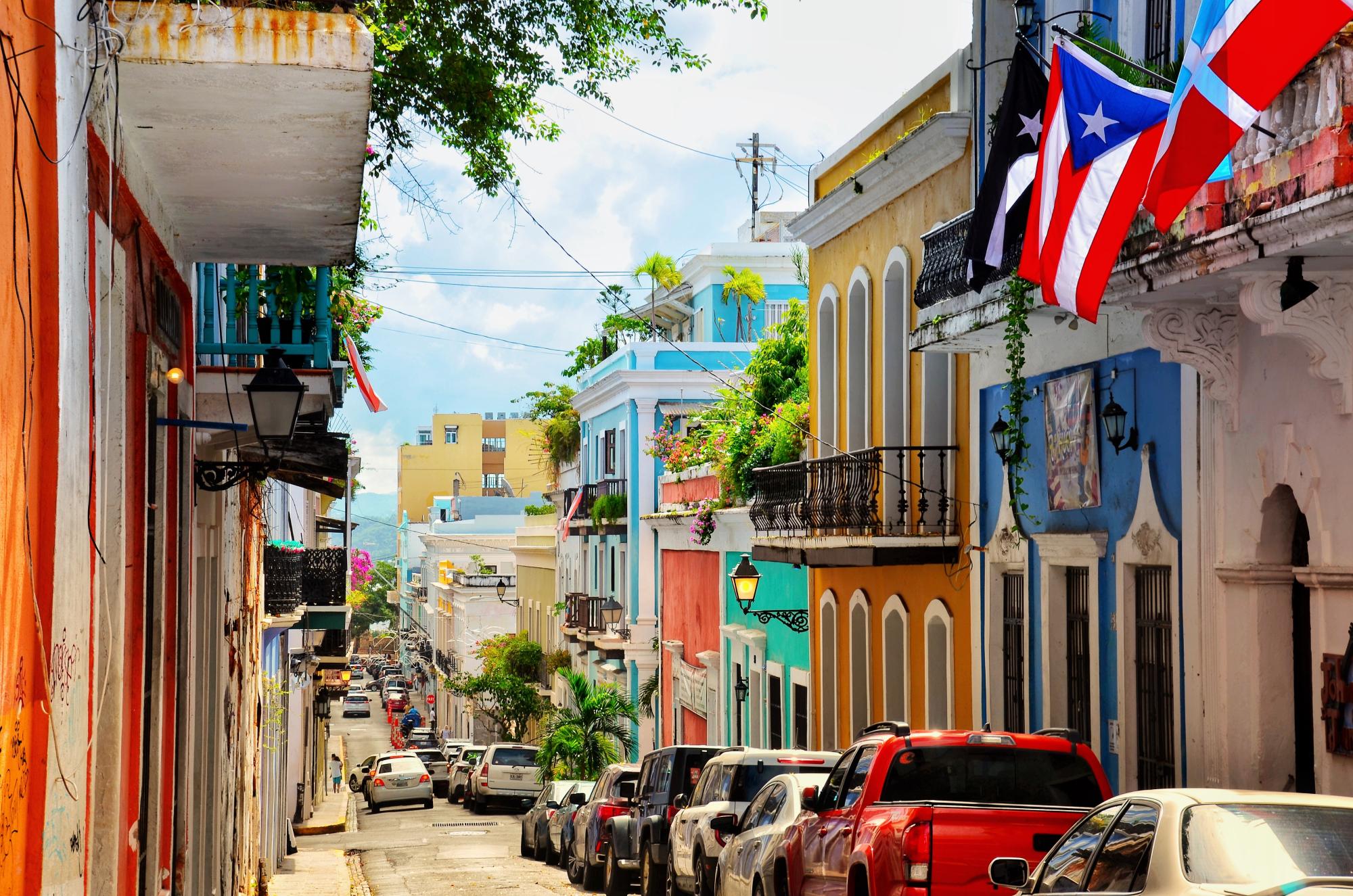A colorful road in San Juan, Puerto Rico, lined with cars and Puerto Rican flags on a sunny day.