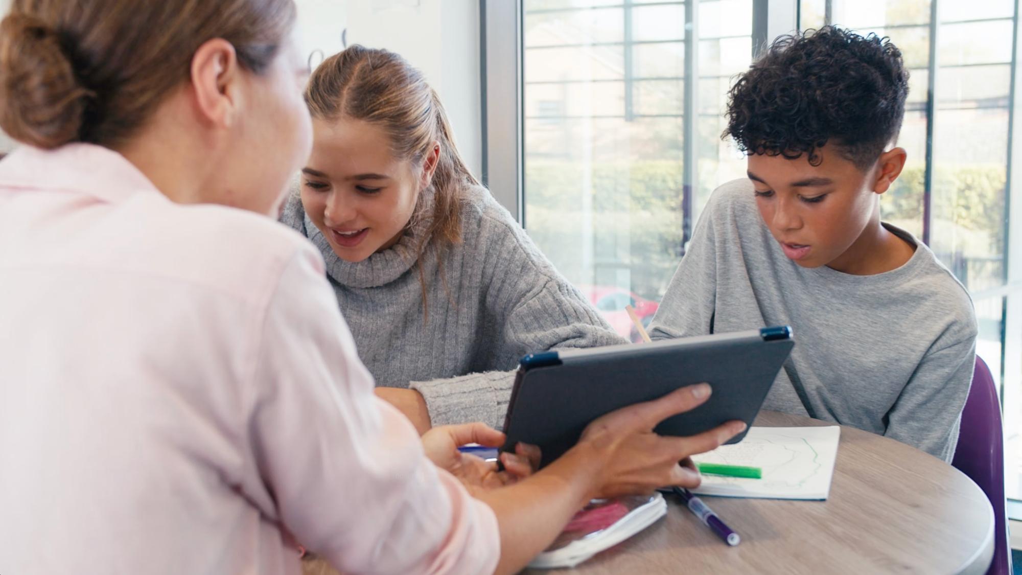 Teacher holds a tablet while a male and female student review 
