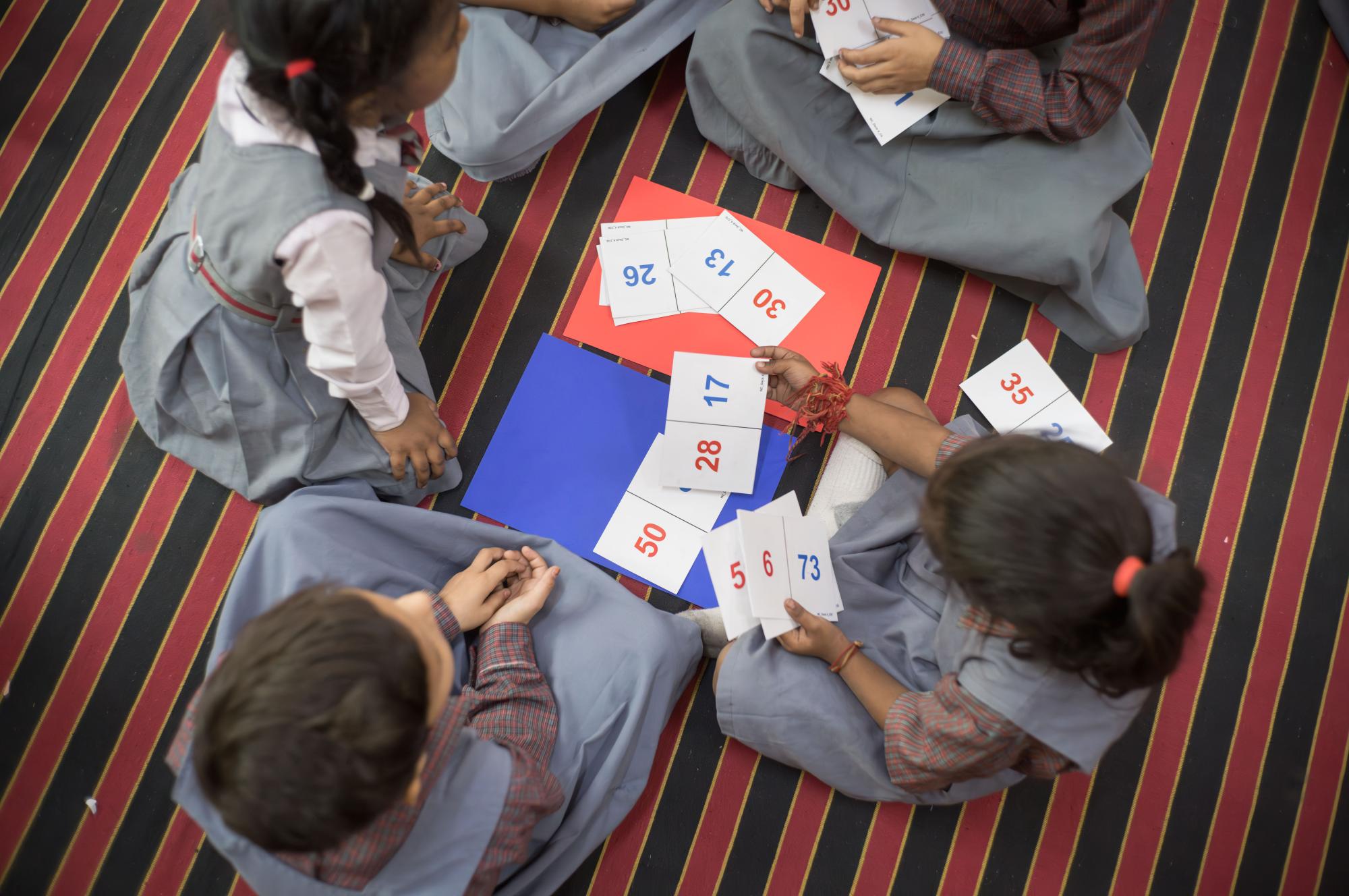 Four students sitting on the ground in a circle playing a math game