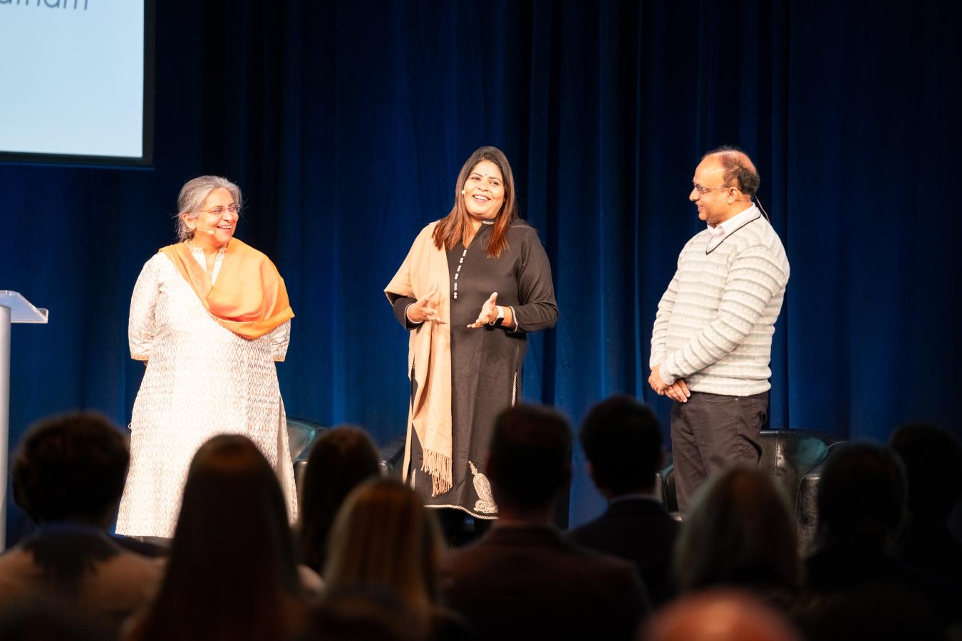 Three people stand on a stage laughing