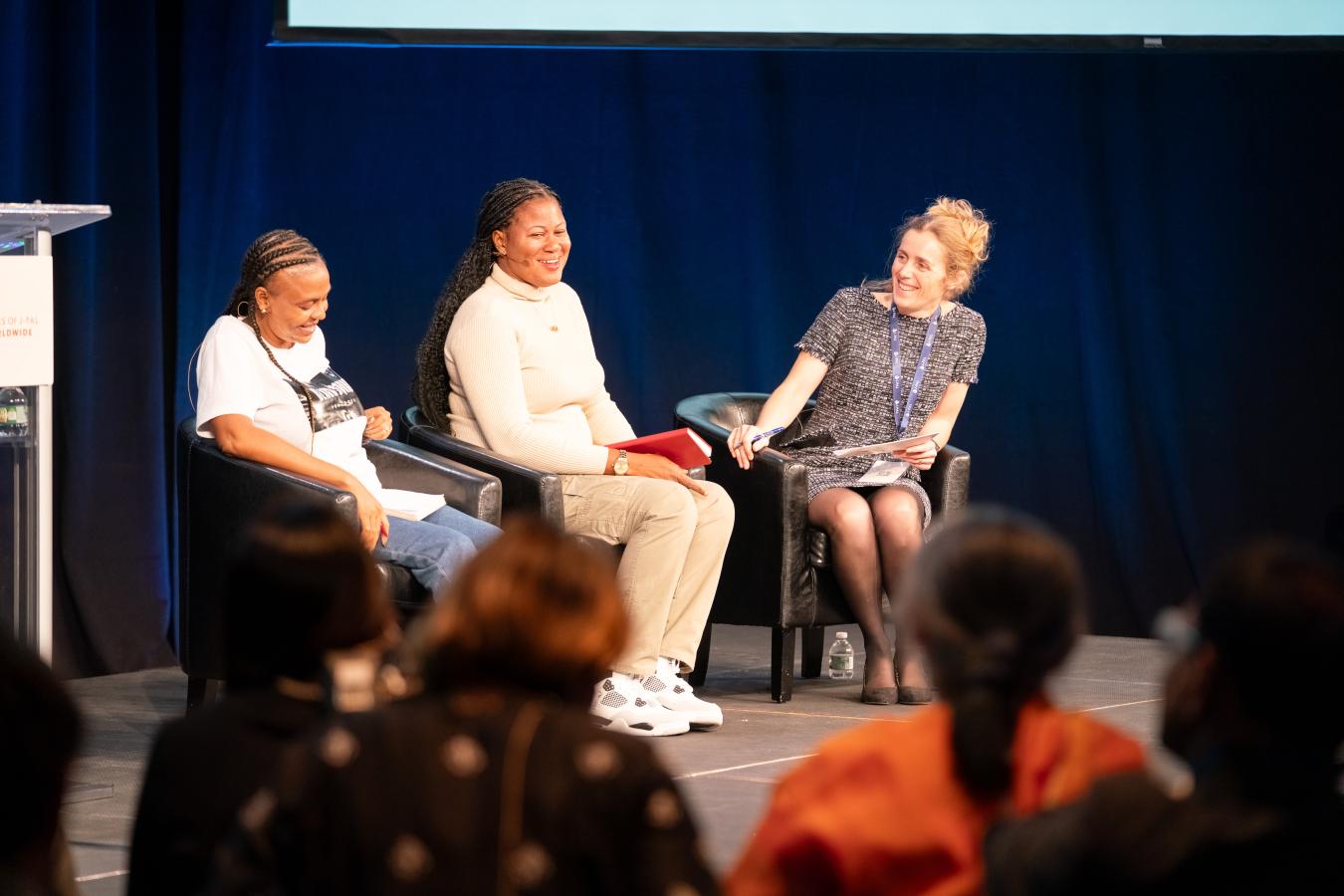 Three women sit on a stage talking