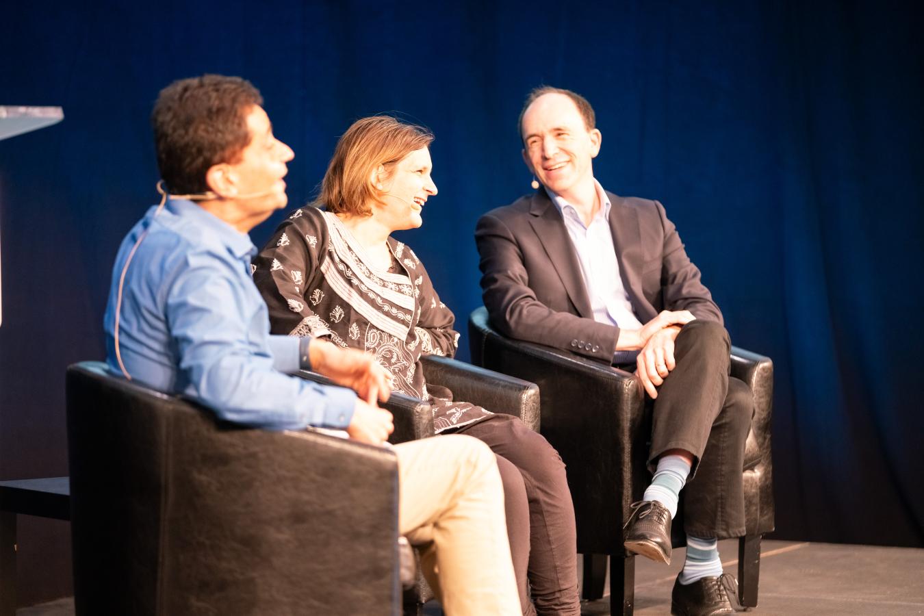 Three people sit in chairs on a stage talking