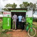 Three people stand at corrugated tin stand advertising mobile services in a field in Kenya