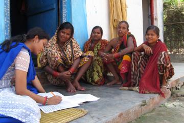 Group of women sit on an outdoor porch while a woman takes notes