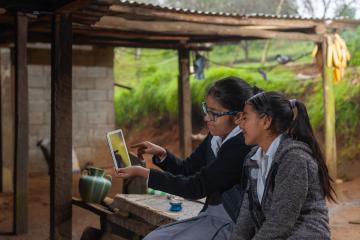 Two female students in school uniform looking at a tablet in Peru.