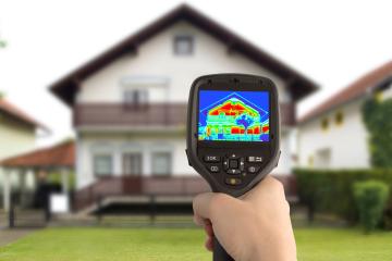 Hand holds up infrared sensor in front of house