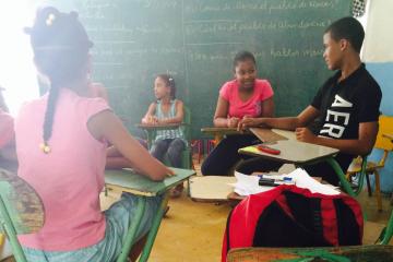 Children sit in schooldesks in front of blackboard