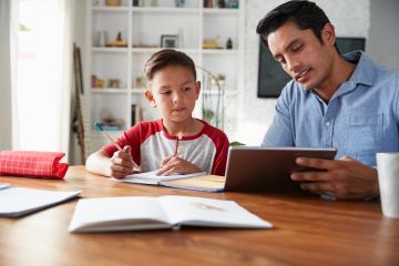 A man shows a tablet to a small child who is doing homework.