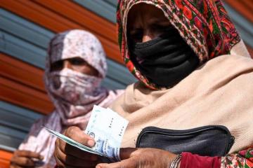 A woman wearing a medical face mask counts rupee notes after collecting cash of financial assistance through a mobile wallet under the governmental Ehsaas Emergency Cash Programme for families in need during a government-imposed nationwide lockdown as a preventive measure against the COVID-19 coronavirus, in Islamabad on April 9, 2020.