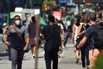 People wearing masks walking along a crowded sidewalk