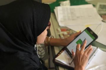 Indonesian woman sits at a table scrolling through a tablet