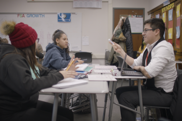 Two high school students sit at desks with their tutor for personalized instruction