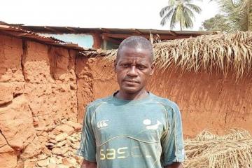 Farmer in a blue T-shirt looking int the camera in front of a brown wall