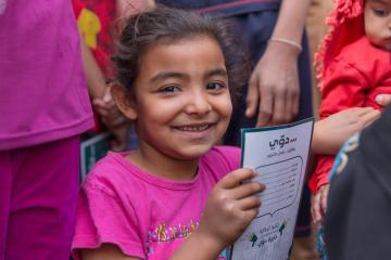 A smiling girl holds a piece of paper.