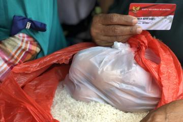 A hand holding a small card resting on top of a bag of rice and a bag of fruit.