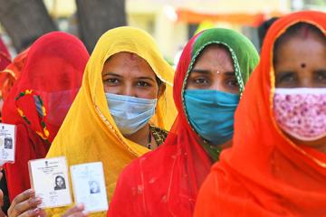 Four women in masks stand in line holding up voter ID cards