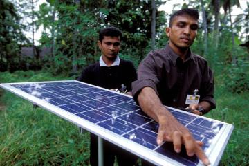 Two men work on a solar panel used for lighting village homes in Sri Lanka