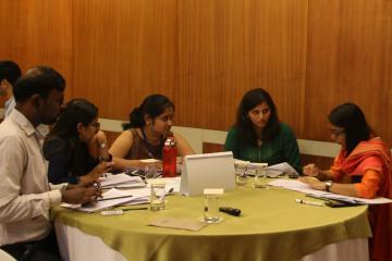 A group of people participating in an impact evaluation training discuss lessons while sitting at a table.