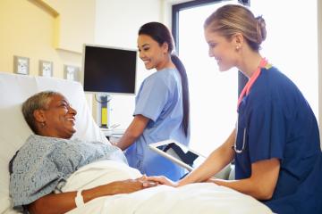 Two nurses help a patient in bed