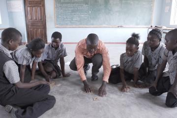 An African teacher teaches six students in a classroom.