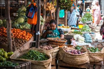 A market vendor sits amid baskets of fresh fruit and vegetables