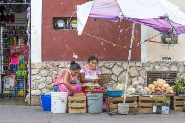 Two female vendors sit in front of a shop. 