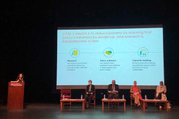 Four panelists sit in front of a screen, while one person presents