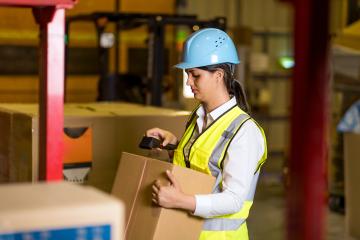 Female worker with helmet and safety vest scanning a box in a factory