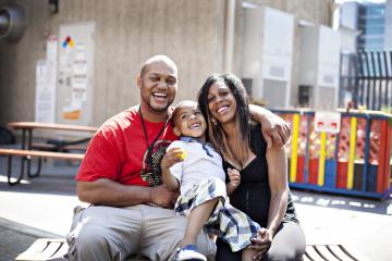 Family sitting on a bench smiling at the camera.