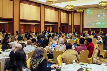 Conference participants sit at round tables watching a presenter on stage at J-PAL SEA's Emerging Challenges in the Environment Landscape: Addressing Climate Change, Sustainability, and Poverty conference.