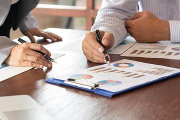 Two individuals holding pens, looking at charts and clipboards