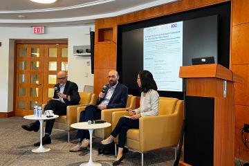 Two men and one woman sit in chairs on a panel.