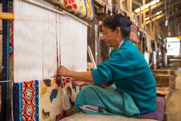 A woman sits and is weaving a rug