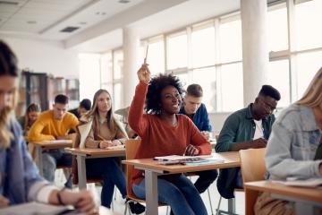 High school students in classroom; one with hand raised