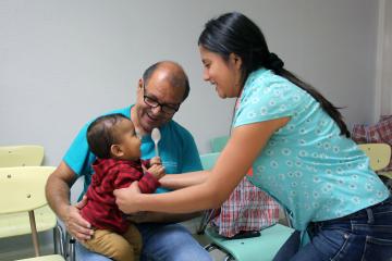 Child laughing with parents and holding a spoon