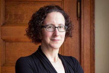 Headshot of Amy Finkelstein, wearing black shirt, in front of wooden door