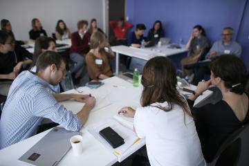 A small room of adult learners sit around tables to discuss a case study.