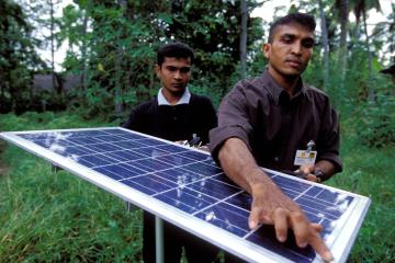 Two technicians install a solar panel in a rural setting in Sri Lanka