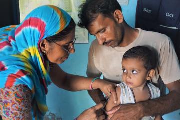 Nurse administers a shot to a child sitting on the father's lap